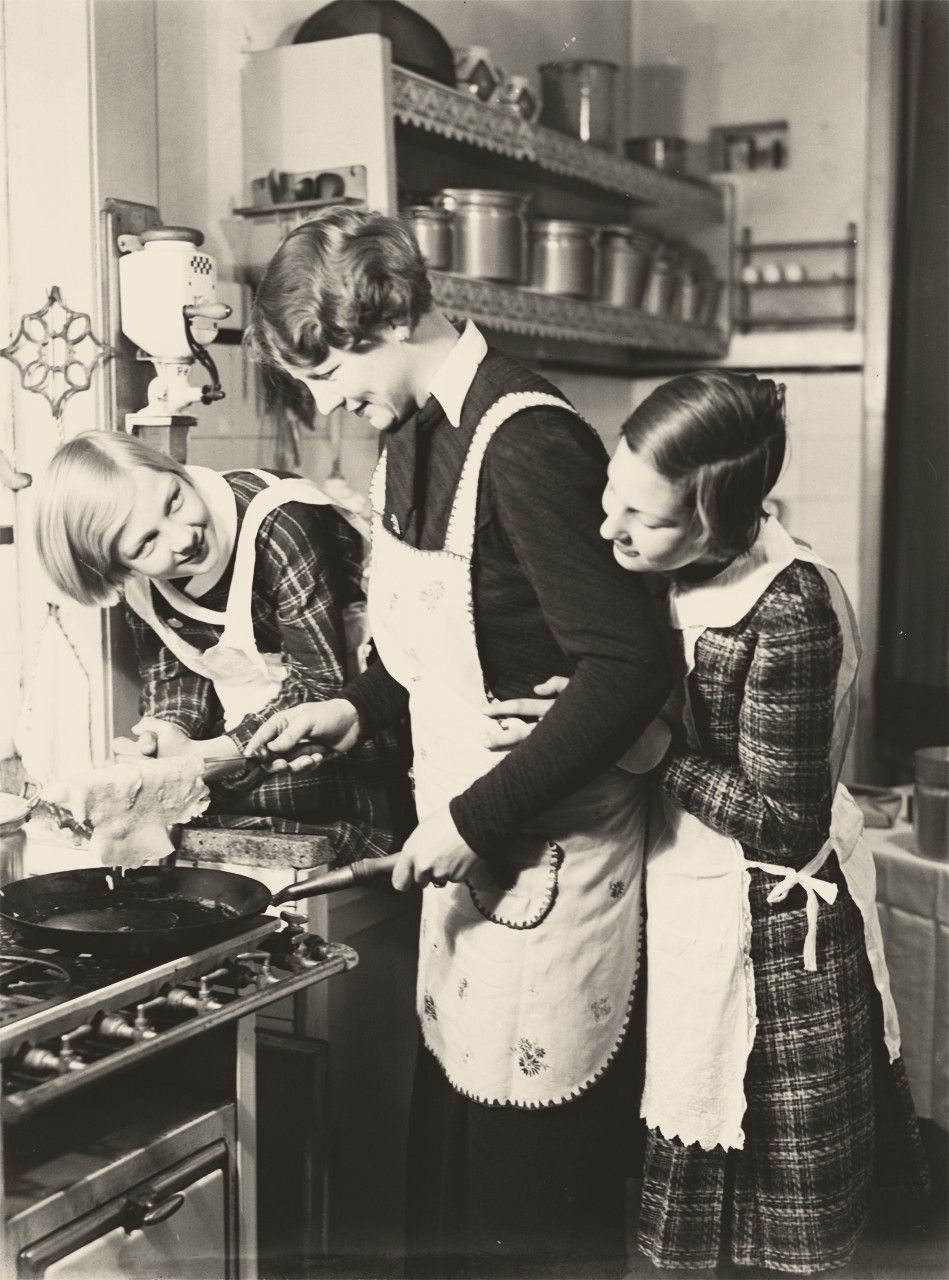 Three women making pancakes in a kitchen, 1930s